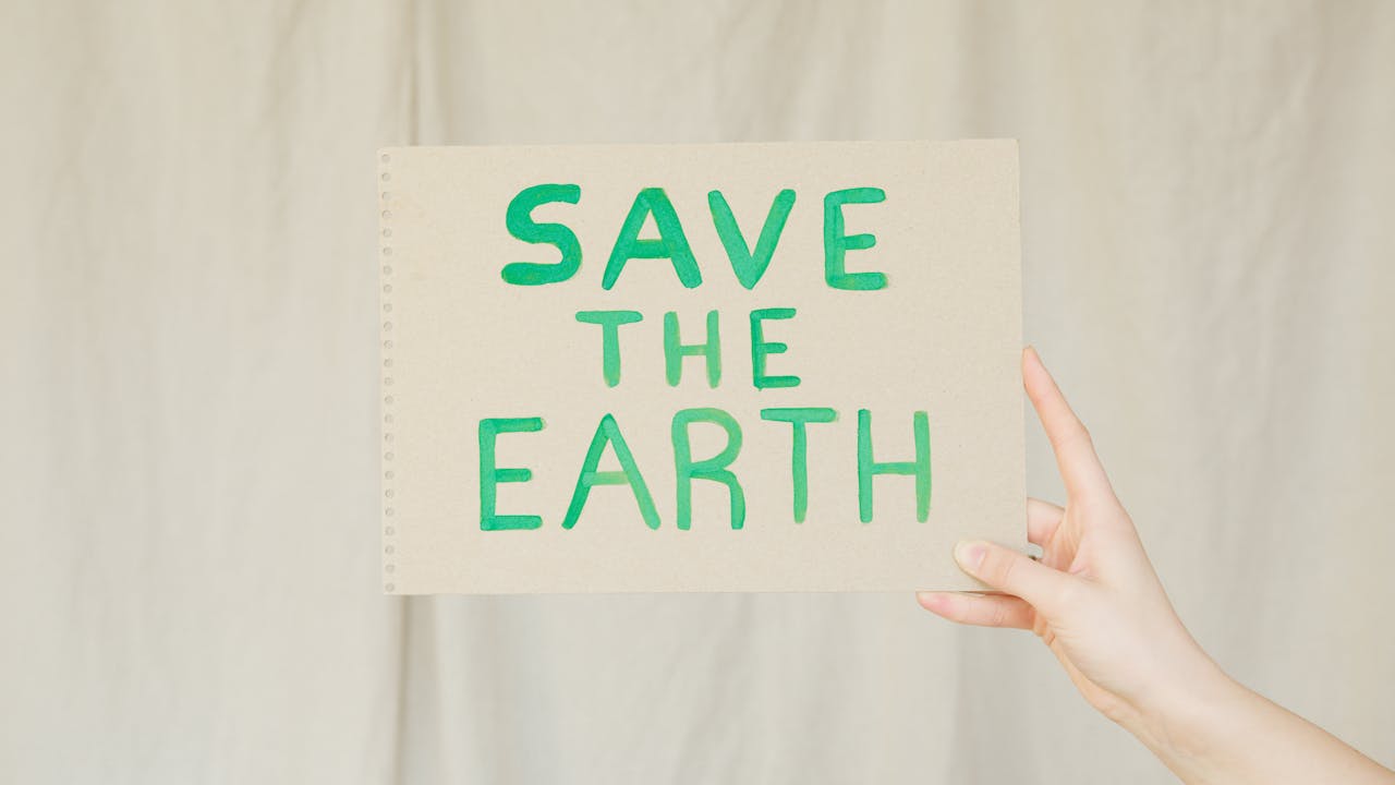 Hand holding a cardboard sign with 'Save the Earth' message advocating environmental conservation.
